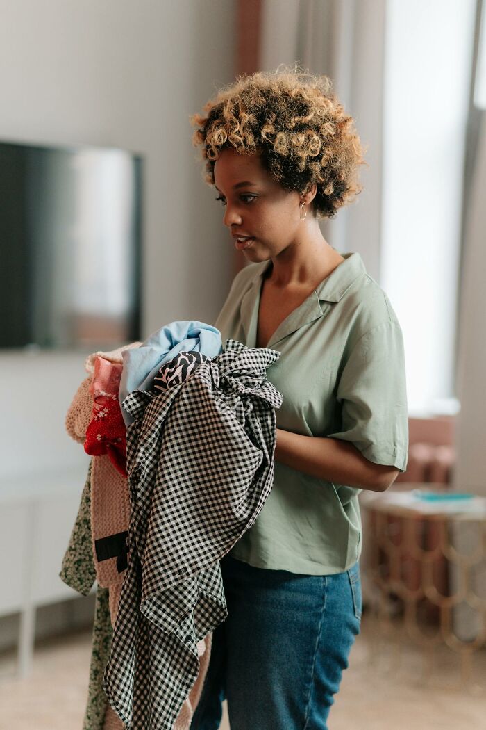 Woman holding a pile of clothes indoors, reflecting on wildest things women let their exes get away with.