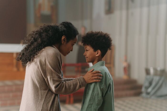 A caring parent kneeling to talk to a young boy with curly hair in an indoor setting, highlighting parenting dynamics.