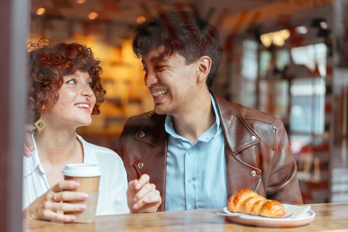 Couple sharing coffee and pastry, smiling and enjoying time together, showing weird things couples started doing.