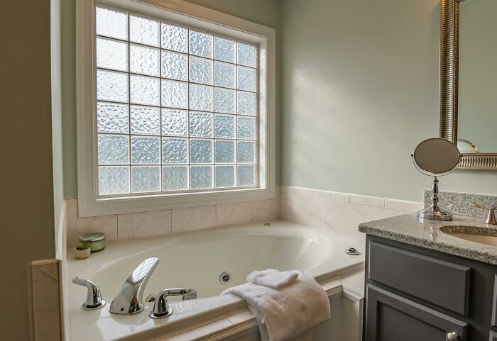 Modern bathroom with a jetted bathtub and frosted window, showcasing uncommon hacks for women living alone comfort.