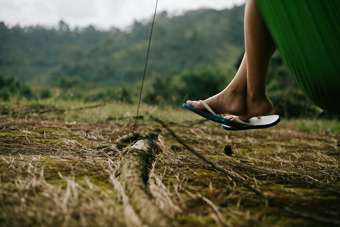 Feet wearing flip-flops hovering above the ground outdoors, capturing a completely normal thing with an irrational ick feeling.