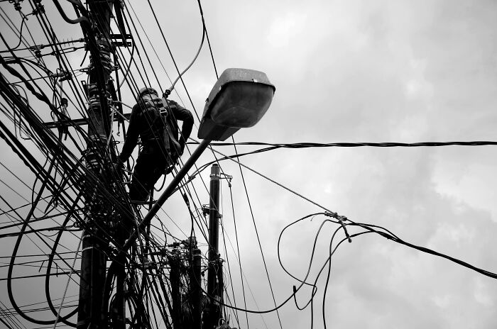 Electrician working on tangled power lines above a streetlight, illustrating hidden costs of buying a home maintenance.