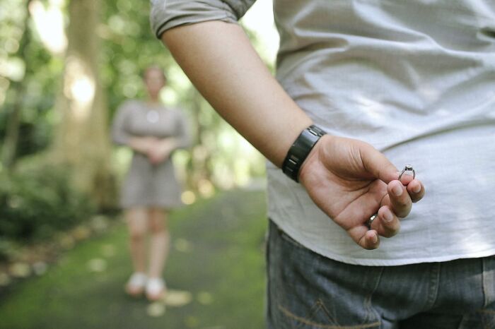 Person hiding engagement ring behind back while standing on a path with partner, illustrating weird things couples started doing.