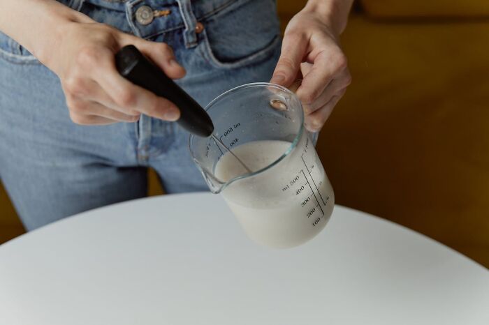 Person using a handheld milk frother and measuring cup, demonstrating everyday items under $300 that improved lives.