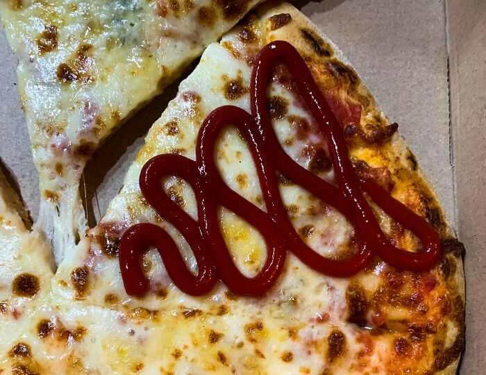 Close-up of pizza slice with ketchup on cheese, illustrating Americans reveal things non-Americans do like breaking spaghetti.