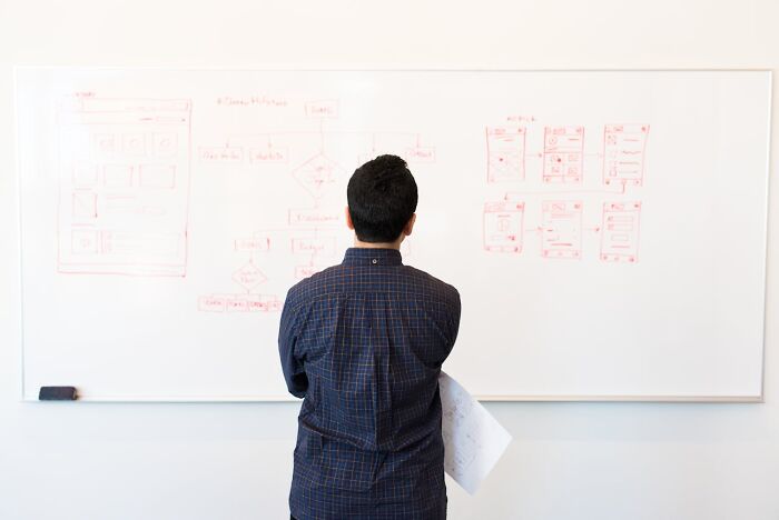 Man standing in front of whiteboard filled with diagrams, reflecting on things male coworkers told women in the workplace.