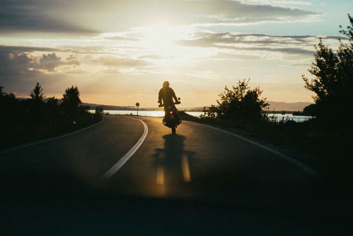 Person riding motorcycle on empty road at sunset, symbolizing life-changing moments and one wrong deed consequences.