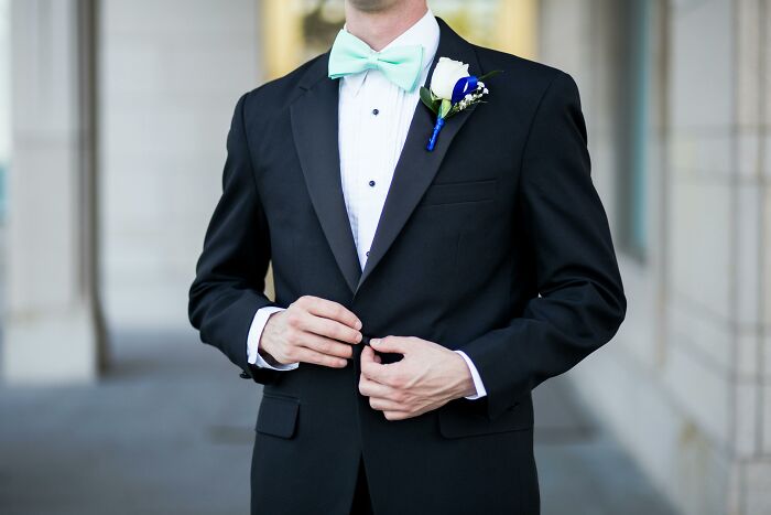 Man wearing a black tuxedo with a mint bow tie and white rose boutonniere, highlighting privilege in a formal setting