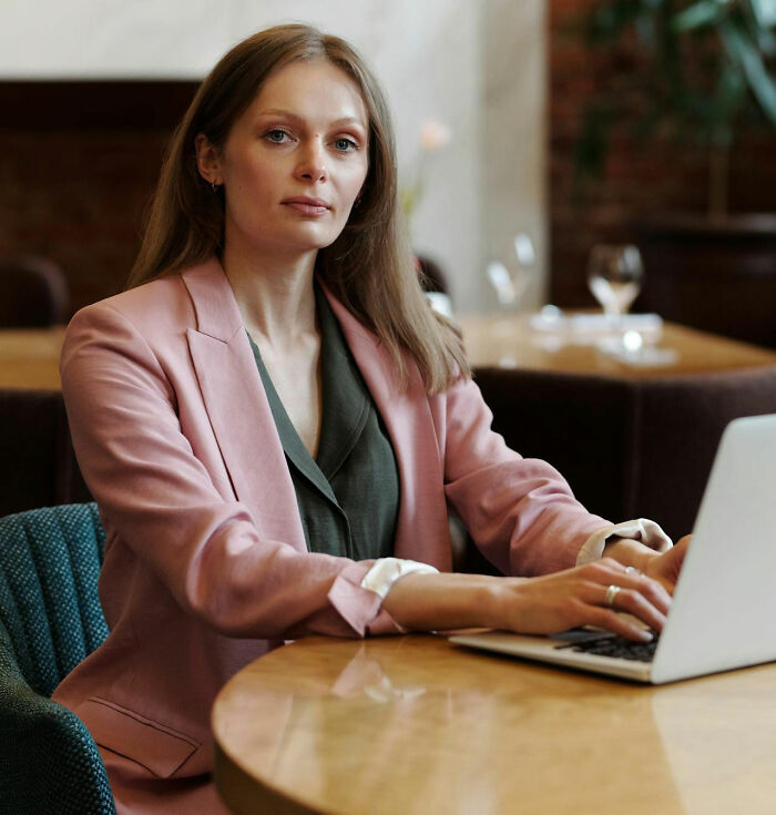 Woman in a pink blazer working on a laptop, representing women sharing stories about male coworkers' insane comments.