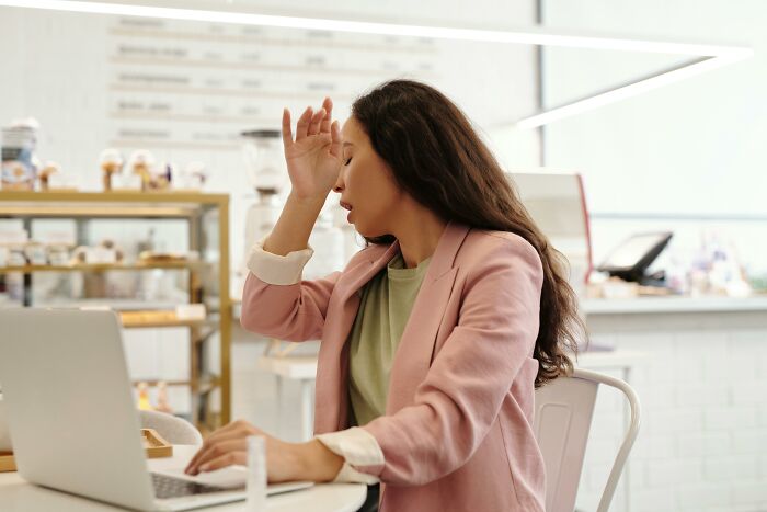 Woman showing an irrational ick reaction while working on a laptop in a bright, modern cafe setting.