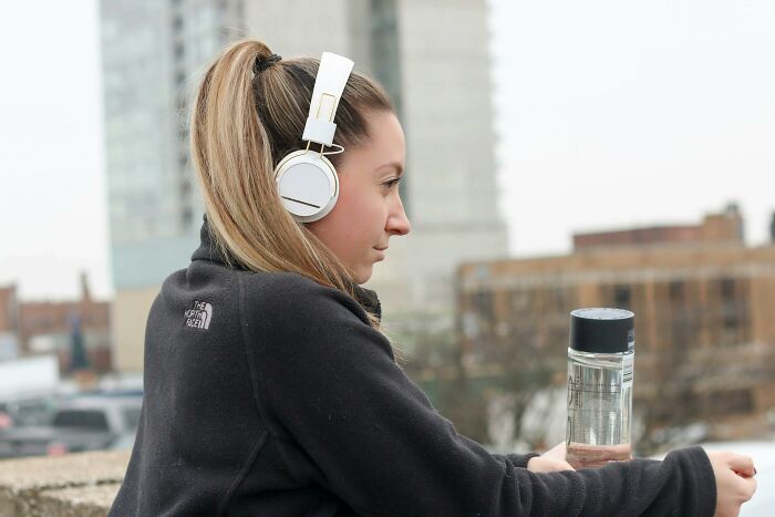 Young woman with headphones in casual wear holding a water bottle outdoors, illustrating casual and harmless looking habits.