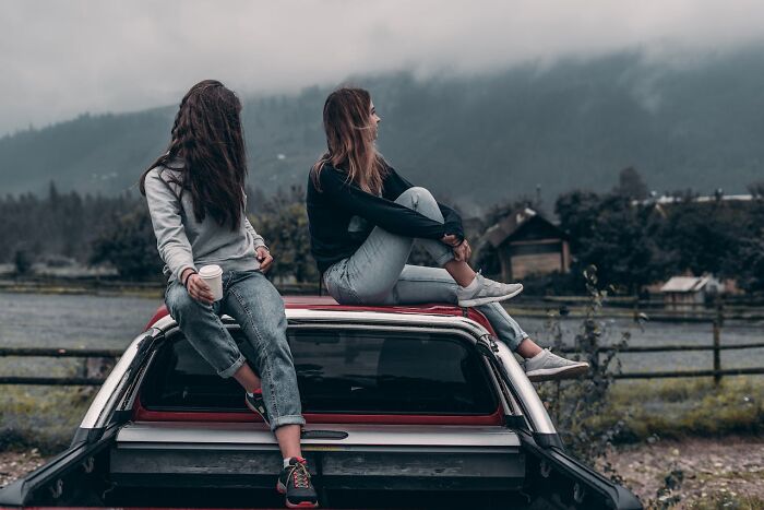 Two women sitting on the back of a car in a rural area, reflecting emotions related to deep shame and secrets in relationships.