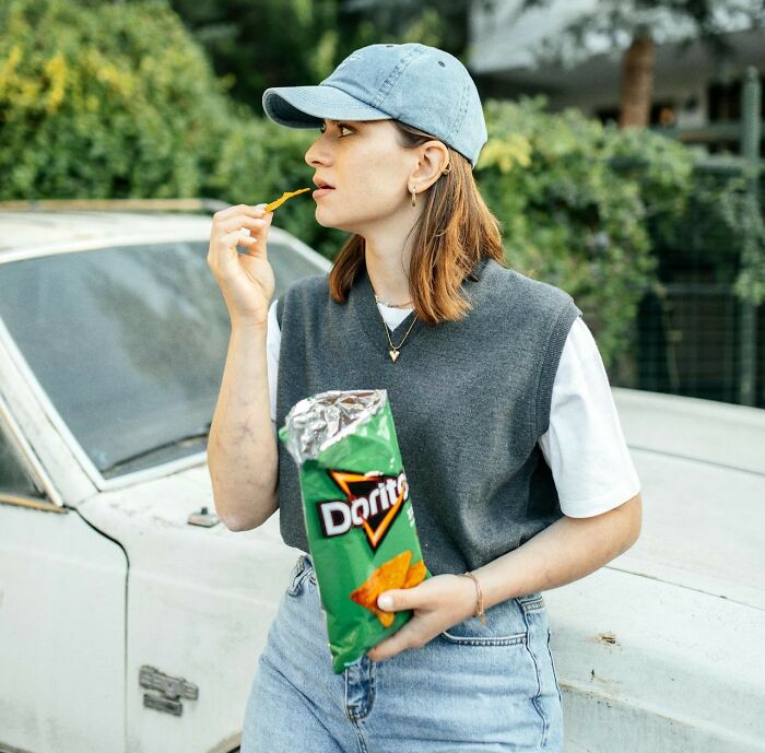 Young woman in casual clothes eating chips outdoors, illustrating a moment before the police got dragged into utter nonsense.