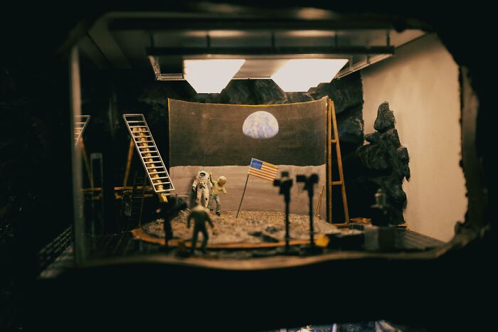 Miniature set of astronauts on a fake moon landing scene, illustrating people still falling for fictional things that were never real.