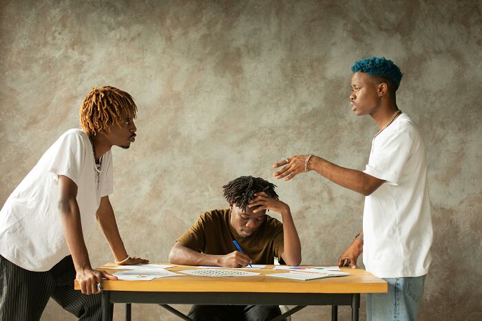 Three young men around a table showing dark truths of human behavior with tense expressions and intense discussion.