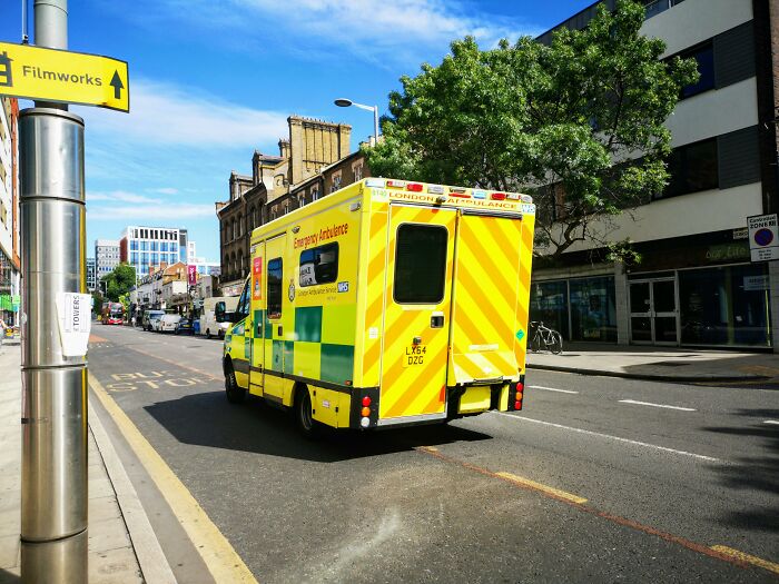 Yellow London ambulance driving on a city street, illustrating public services in the UK.