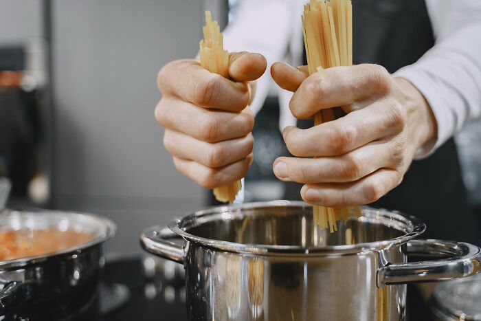 Hands holding spaghetti over a pot, illustrating a common mistake Americans say non-Americans make with Italian food.