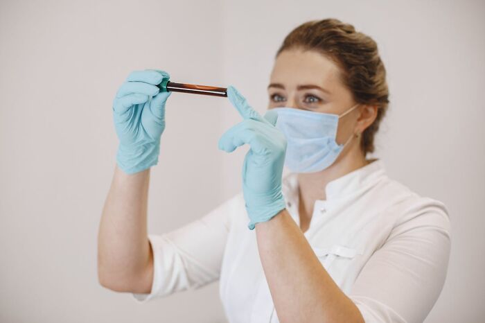 Medical professional wearing a mask and gloves examining a test tube, representing unresolved personal mysteries about people.