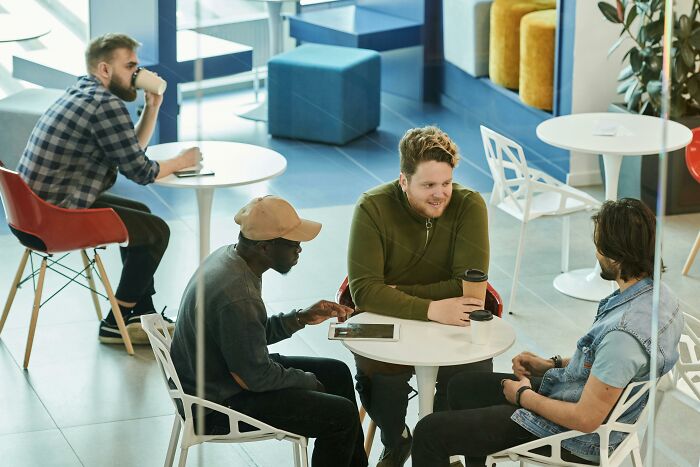 Three men discussing at a cafe table while another person drinks coffee, illustrating moments when people forget their privilege.