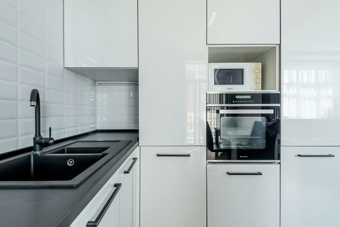 Modern kitchen with black sink and faucet, white cabinets, and built-in microwave and oven, showing a completely normal thing.