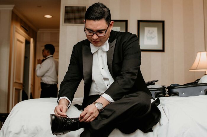 Man in a tuxedo sitting on a bed tying shoes, depicting moments related to hooking up with a friend’s parent.