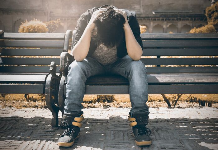 Teen sitting on outdoor bench with head in hands, illustrating pain and distress caused by terrible parents.