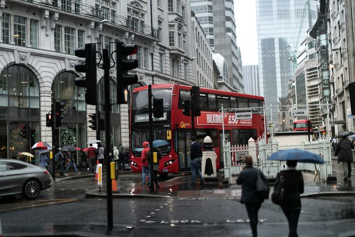 Busy rainy London street scene with red double-decker bus and pedestrians holding umbrellas in the UK city center.