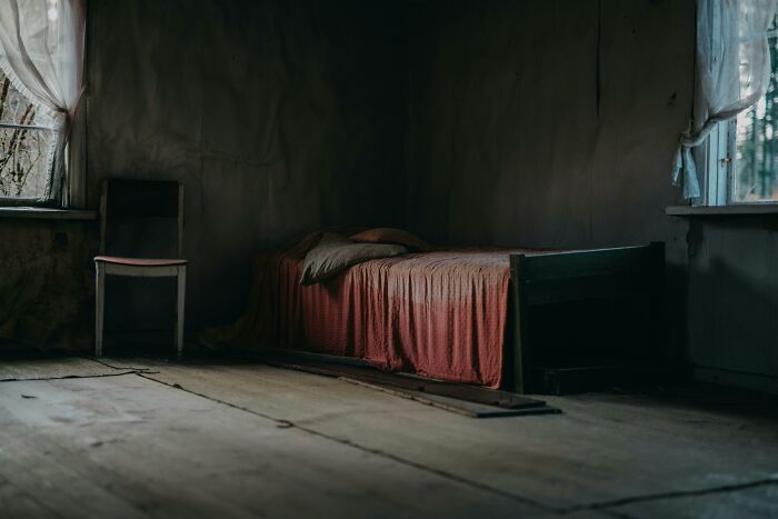 Dimly lit abandoned room with an old bed and chair, evoking scary and unsettling Wikipedia article themes.