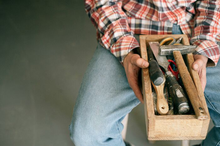 Person holding a wooden toolbox filled with tools representing hidden costs of buying a home and home maintenance expenses