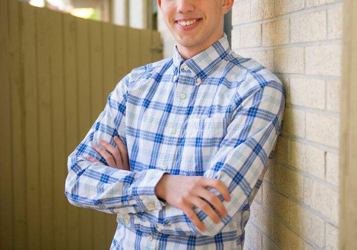 Young man in a plaid shirt leaning against a wall, smiling and revealing what happens after hooking up with a friend’s parent.