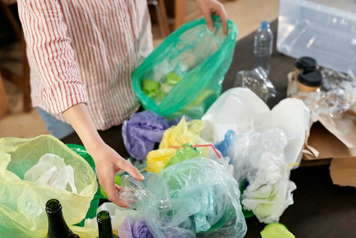 Person sorting recyclable plastic waste into colored bags, showing middle class lifestyle habits and environmental care.
