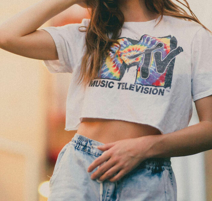 Young woman wearing a vintage MTV crop top and denim shorts, capturing a moment of nostalgic 90s fashion style.