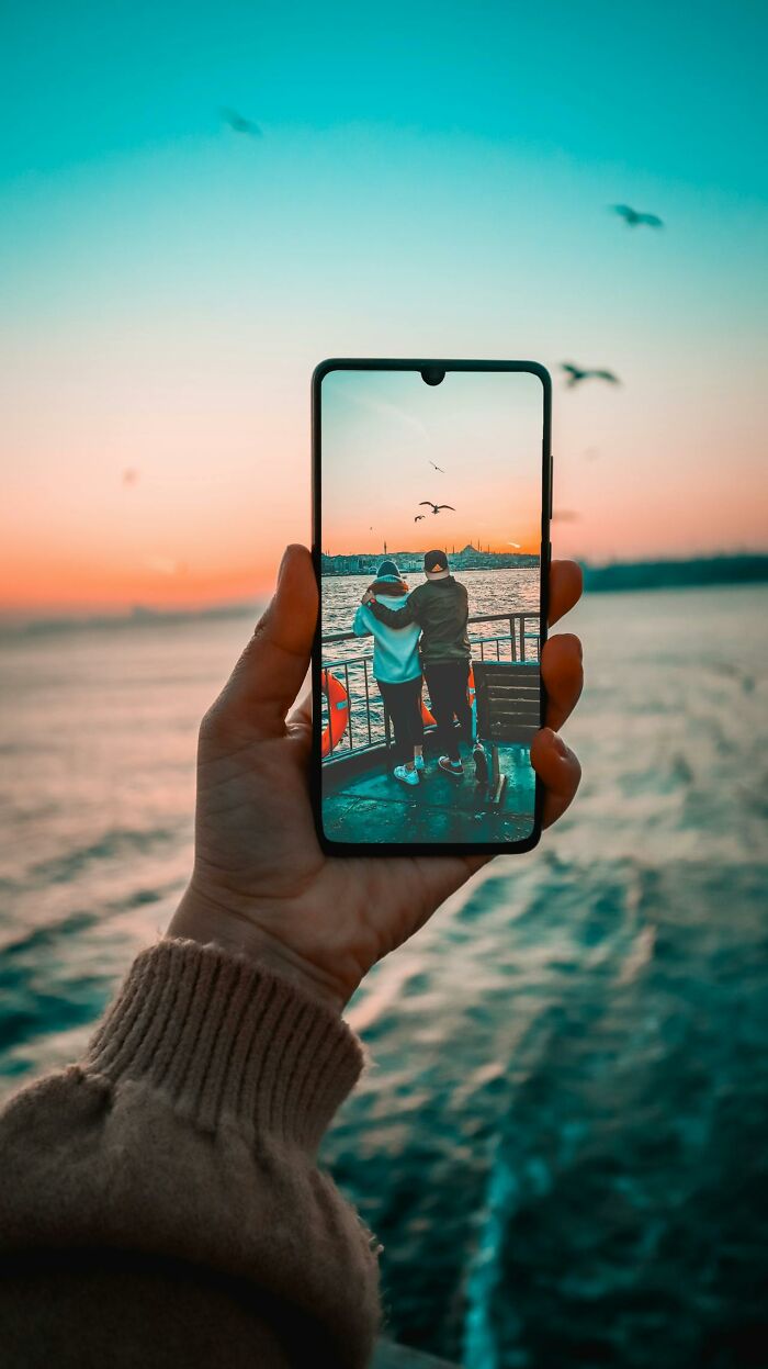 Hand holding phone displaying couple by water at sunset, illustrating wildest things women let their exes get away with.