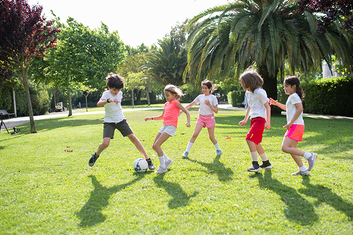 Children playing soccer in a park, illustrating a pediatrician refusing to play nanny during a family getaway.