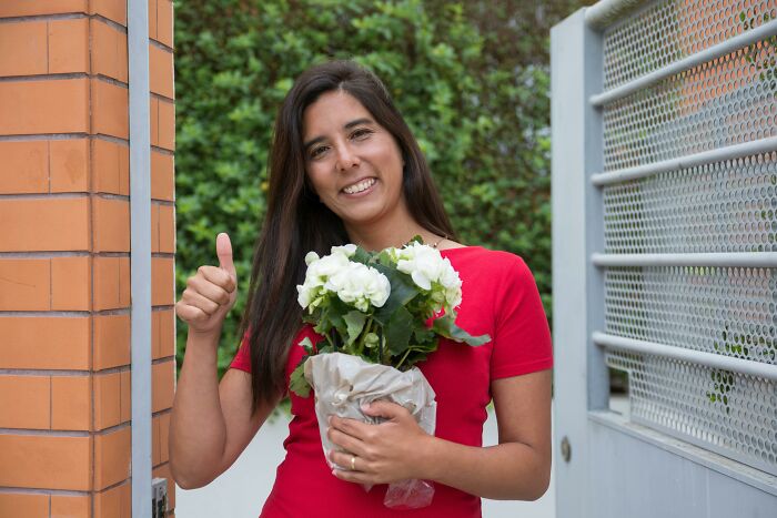 Woman living alone smiling outdoors holding a bouquet of flowers and giving a thumbs up gesture.