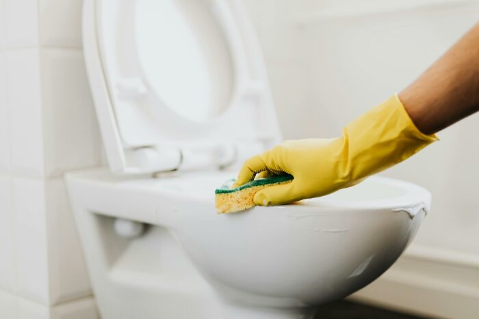 Hand in yellow glove cleaning toilet bowl with sponge, symbolizing dealing with coworker diabolical things to report HR.