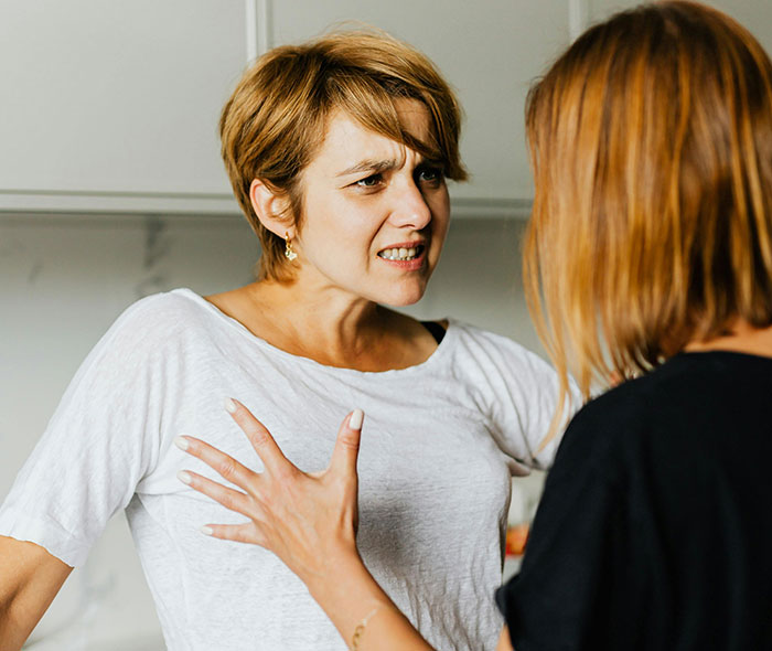 Woman with short hair arguing with a neighbor in a kitchen, highlighting clueless neighbors in babysitting disputes.