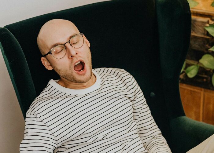 Man with glasses and striped shirt yawning in a chair, illustrating one of the weird things couples started doing.