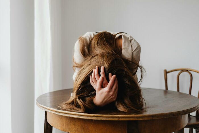 Person hiding face in hands on wooden table, conveying a completely normal thing causing irrational ick feelings.