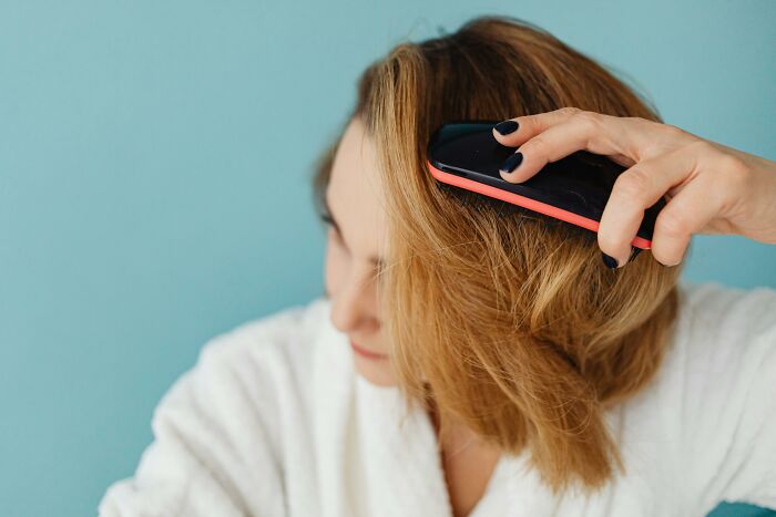 Woman in white robe brushing hair at home, reflecting on coworker diabolical things to report to HR.