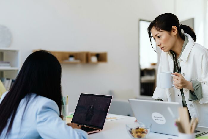 Two women working on laptops in a modern office, highlighting casual habits that may be damaging in the long run.