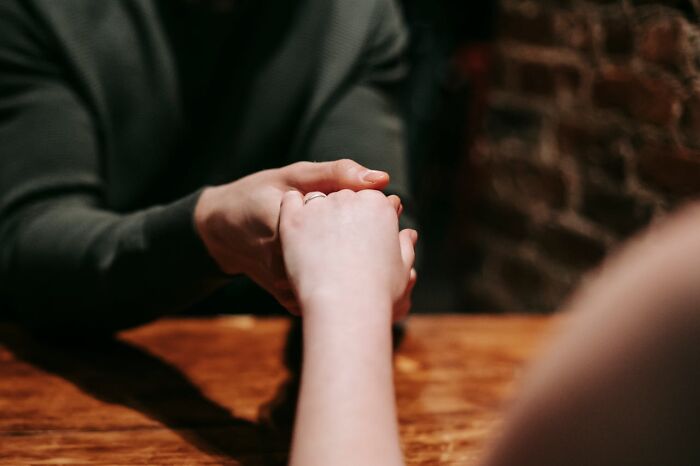 Two people holding hands across a wooden table, expressing emotion and deep connection in a private moment.