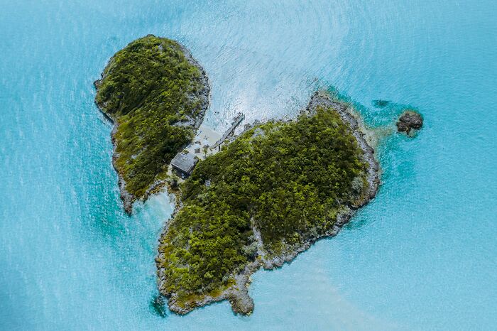 Aerial view of a private island surrounded by turquoise water, highlighting luxury and privilege in the real world.