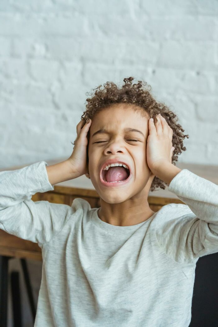Upset child covering ears and yelling indoors, illustrating emotional distress caused by terrible parents revealed online.