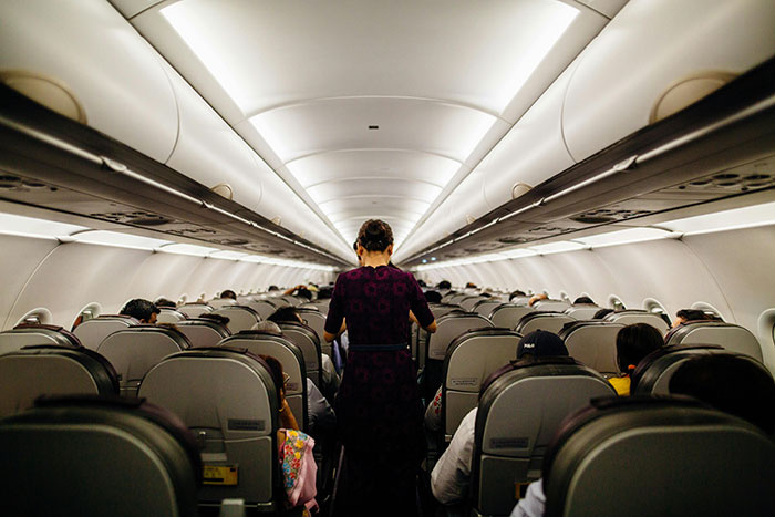 Flight attendant walking down airplane aisle surrounded by passengers in seats, illustrating airplane seat conflict and children scenario.
