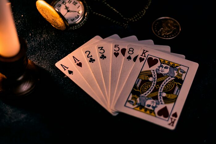 A hand of playing cards fanned out on a dark surface alongside a pocket watch and a candle, symbolizing one wrong deed.
