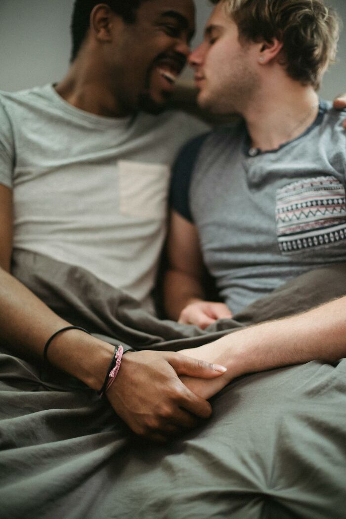 Two men holding hands and leaning close, sharing an intimate moment about hooking up with a friend’s parent.