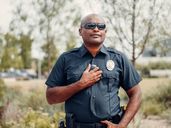 Police officer standing outdoors wearing sunglasses, holding a radio, symbolizing authority in unhinged ways to get back.