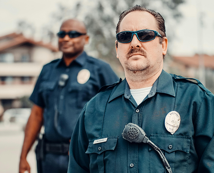 Two police officers in uniform, one prominently wearing sunglasses, responding to a playground mishap involving a dad.