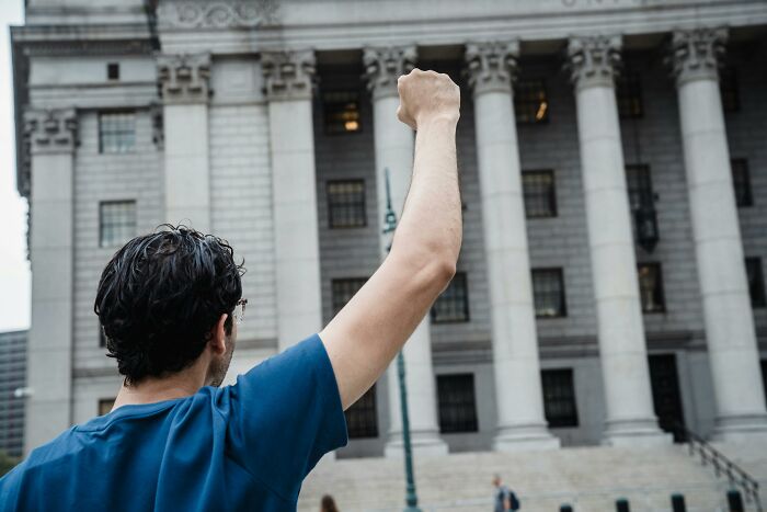 Man raising fist in front of a large government building representing people falling for fictional things never real.
